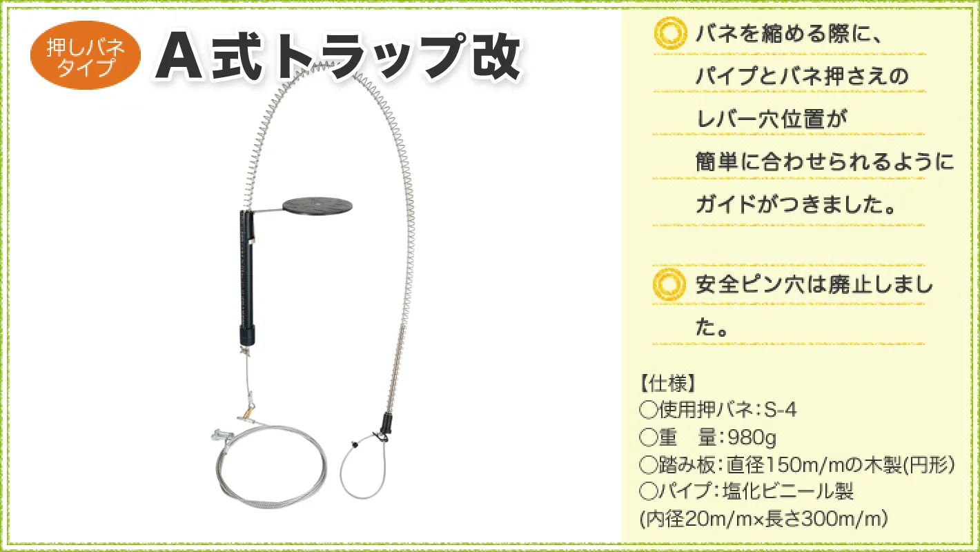 押しバネタイプの「A式トラップ」を紹介する商品画像。左側に長い押しバネ、黒い筒状部品、円形の踏み板、ワイヤー類を備えた罠を配置。右側には、バネを縮める際にパイプとバネ押さえのレバー穴位置を合わせやすくするガイドを追加し、安全ピン穴を廃止したことを説明。仕様は使用押しバネS-4、重量980g、直径150mmの木製円形踏み板、内径20mm・長さ300mmの塩化ビニール製パイプ。